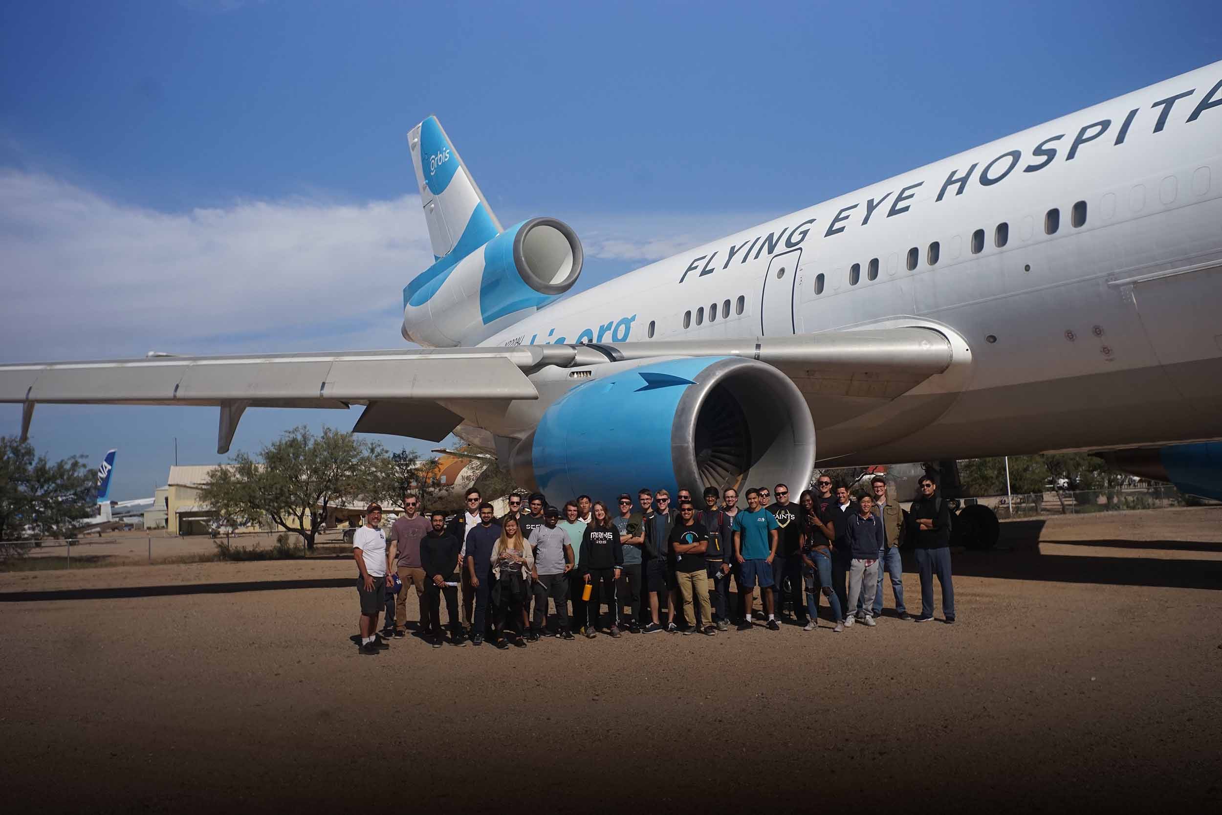 Timothy Takahashi stands with about 50 other people next to the jet engine of a large plane with 